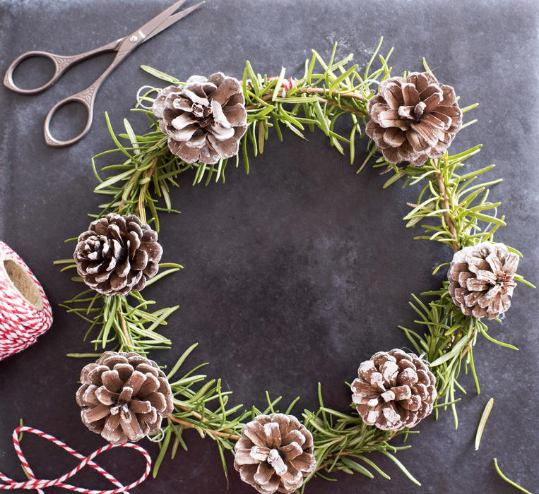 Handmade Christmas crafts with pine wreath with fresh green foliage and cones alongside scissors and twine