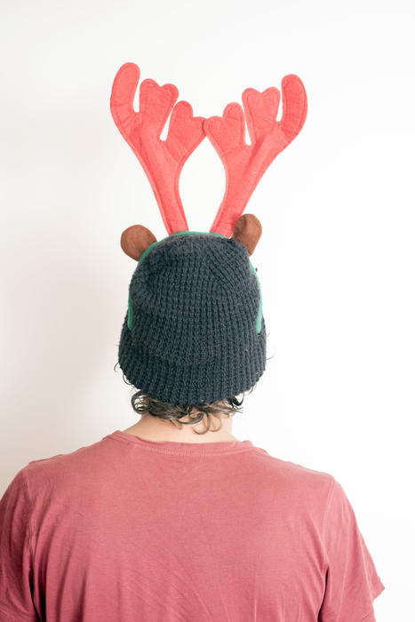 Person wearing a red Christmas reindeer hat with antlers viewed from the rear over white