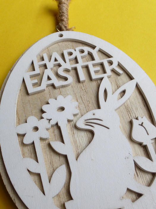Cute rustic hand crafted wooden Happy Easter medallion with bunny rabbit and flowers in a close up cropped view on yellow