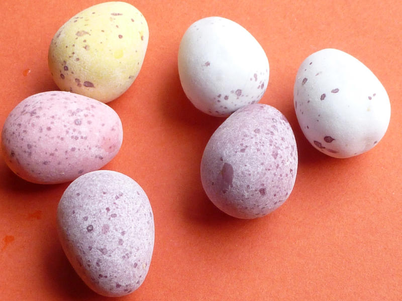 Mini sugar-coated candy Easter eggs in pastel colors to resemble quail eggs scattered on an orange background for the holiday season