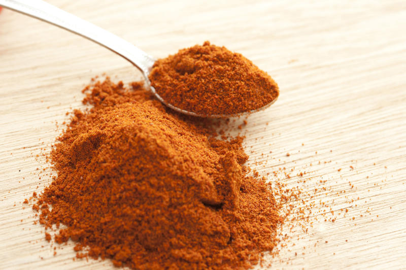 Spoonful of ground dried paprika spice made from sweet bell peppers held over a heap on a wooden chopping board with copy space