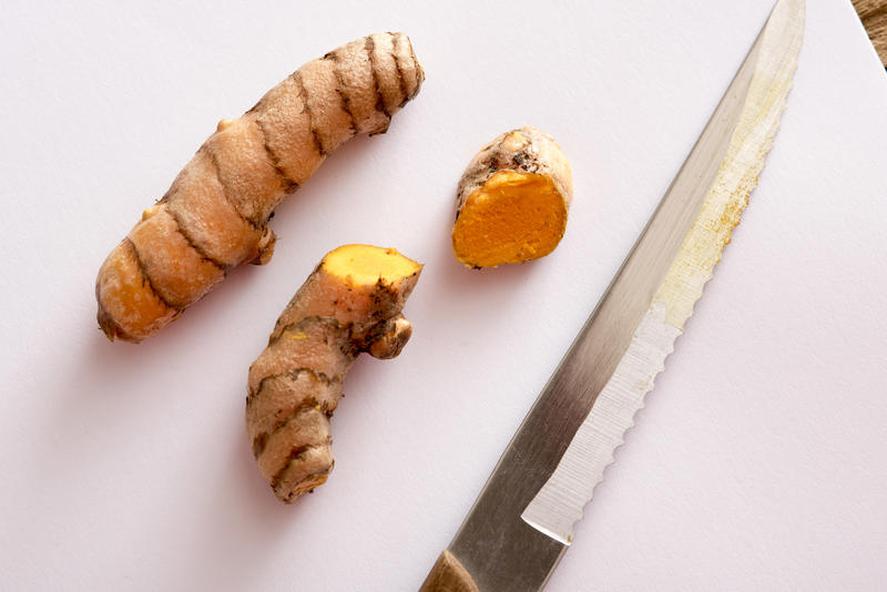 A close up of sliced turmeric and a serrated knife on a white chopping board.