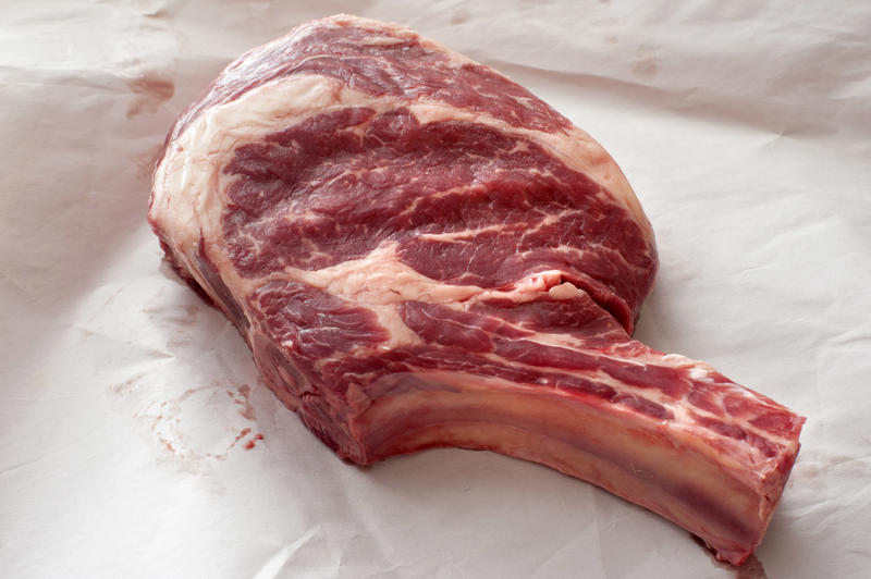 Piece of uncooked meat ribeye steak in close-up on white paper surface