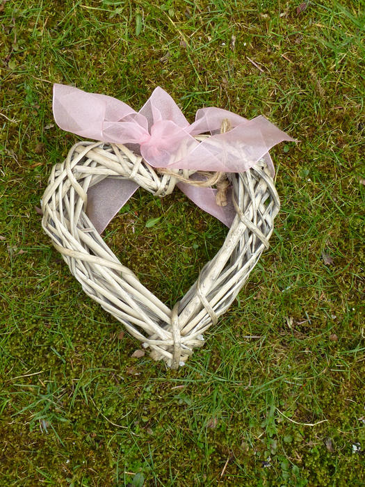 Wicker heart with pink ribbon on fresh grass in the spring, viewed from above in full frame background concept
