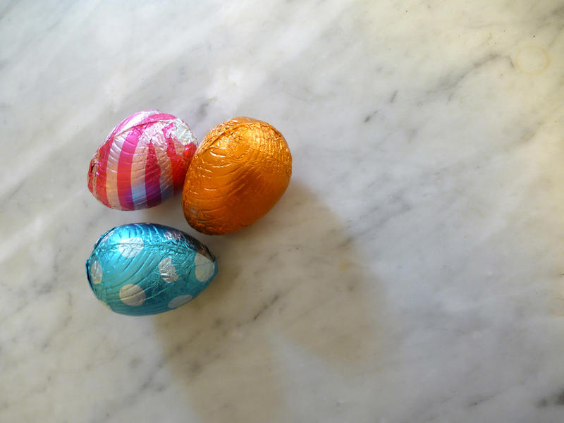 Three chocolate eggs in colorful foil for Easter decorations isolated on white marble surface background