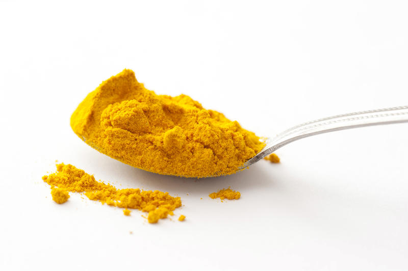 Full spoon of yellow turmeric powder spice viewed from the side in close-up on white surface