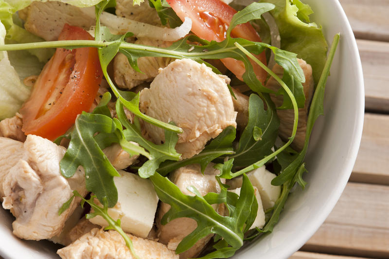 Healthy warm chicken salad topped with rocket and sliced tomatoes in a close up view in a bowl