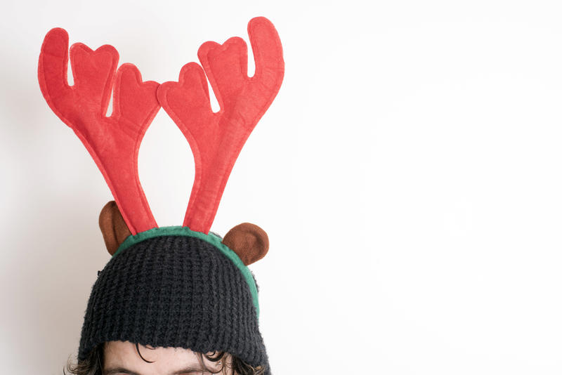 Person wearing a pair of festive red reindeer antlers to celebrate Christmas on a knitted hat in close up with copy space